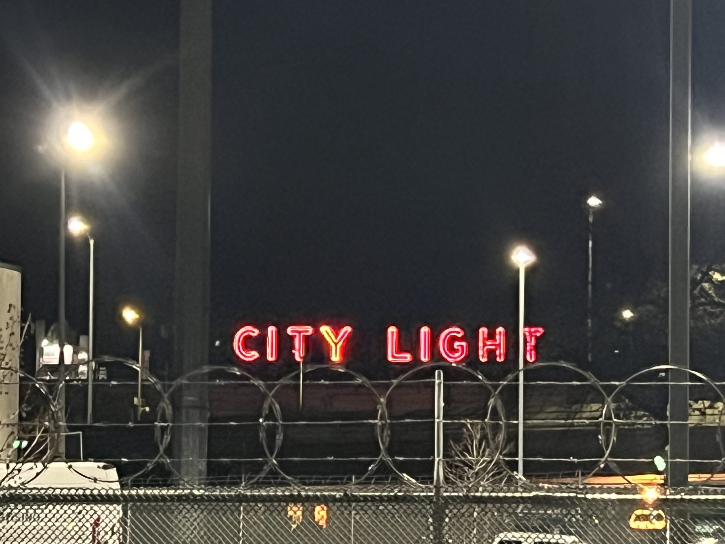 CITY LIGHT marquee at the edge of the gallery, neon catching the wet pavement.
