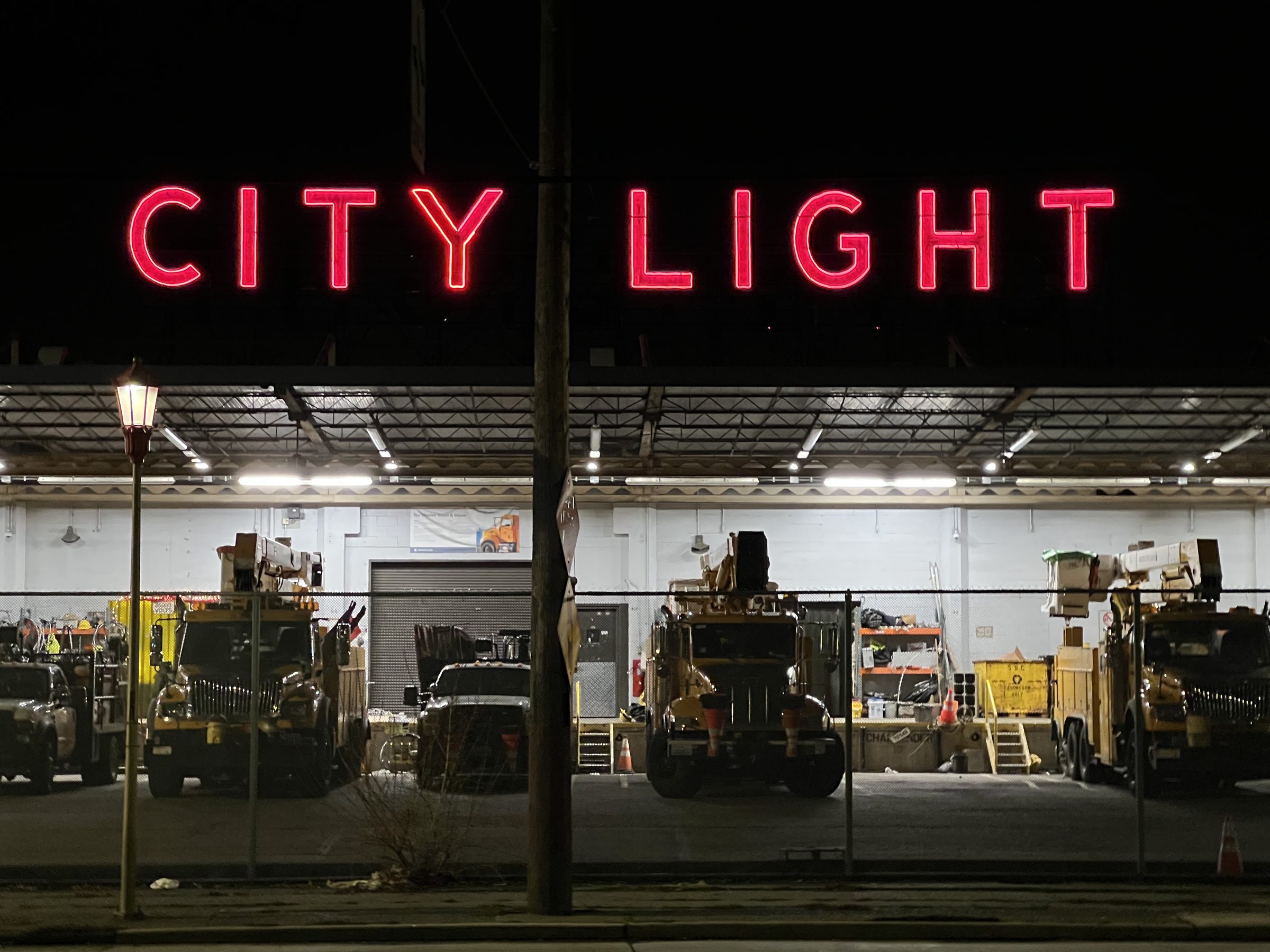 The Seattle City Light maintenance depot at night in Georgetown — the red neon CITY LIGHT sign across the roofline, bucket trucks parked in the bays below.