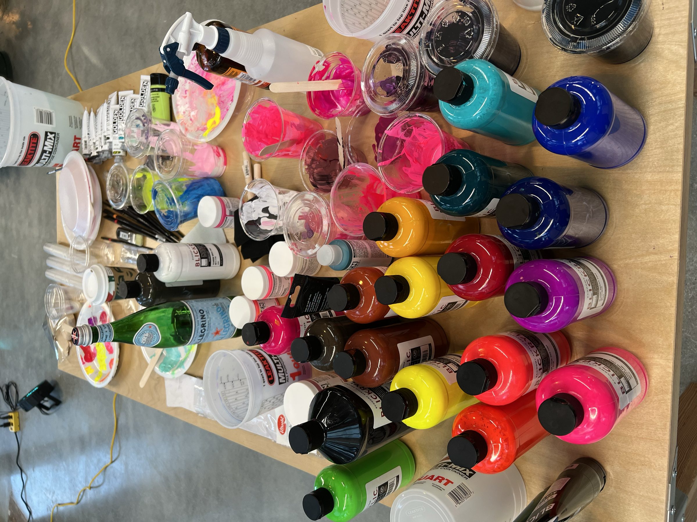 Overhead view of paint bottles and palette — the saturated colors of neon translated to acrylic.