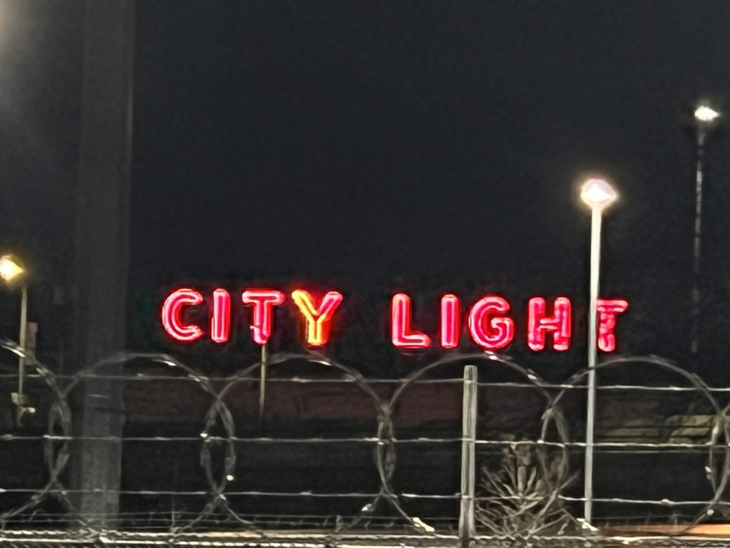 The Seattle City Light neon viewed across an industrial razor-wire fence — Georgetown at night.