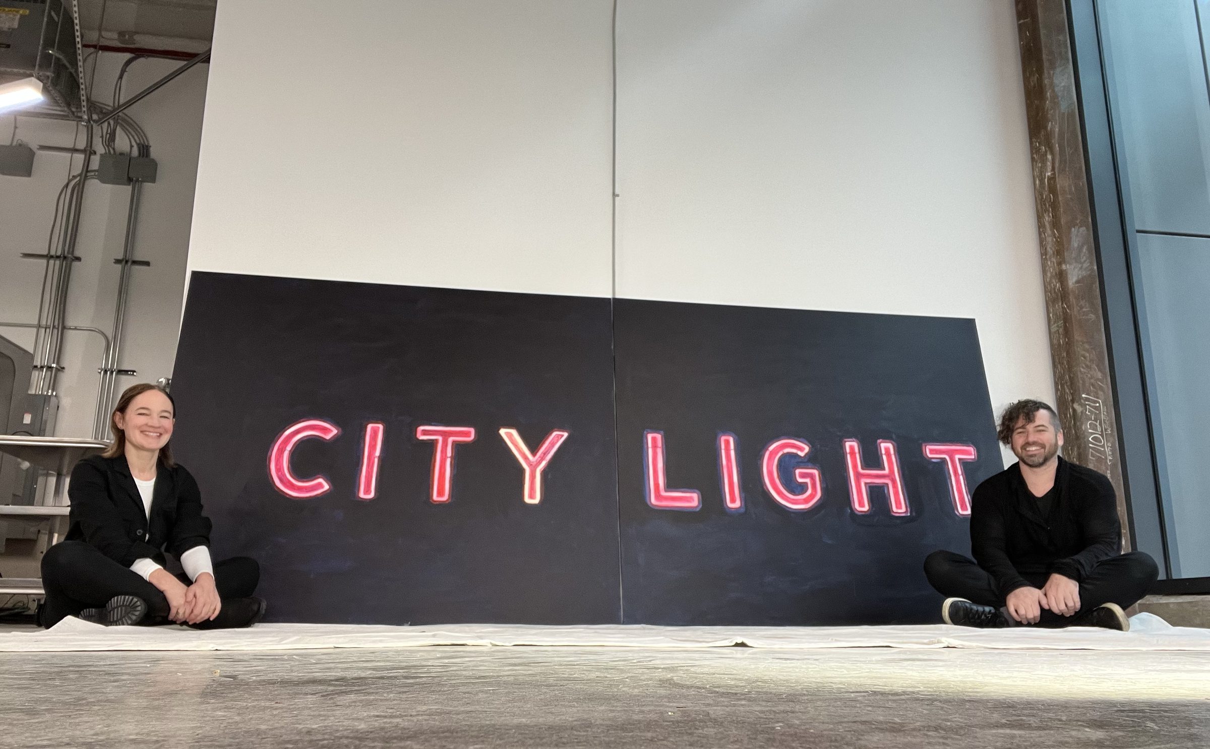 Joshua Borsman and Jacqueline Goldberg sitting on either side of the finished CITY LIGHT diptych on the studio floor.