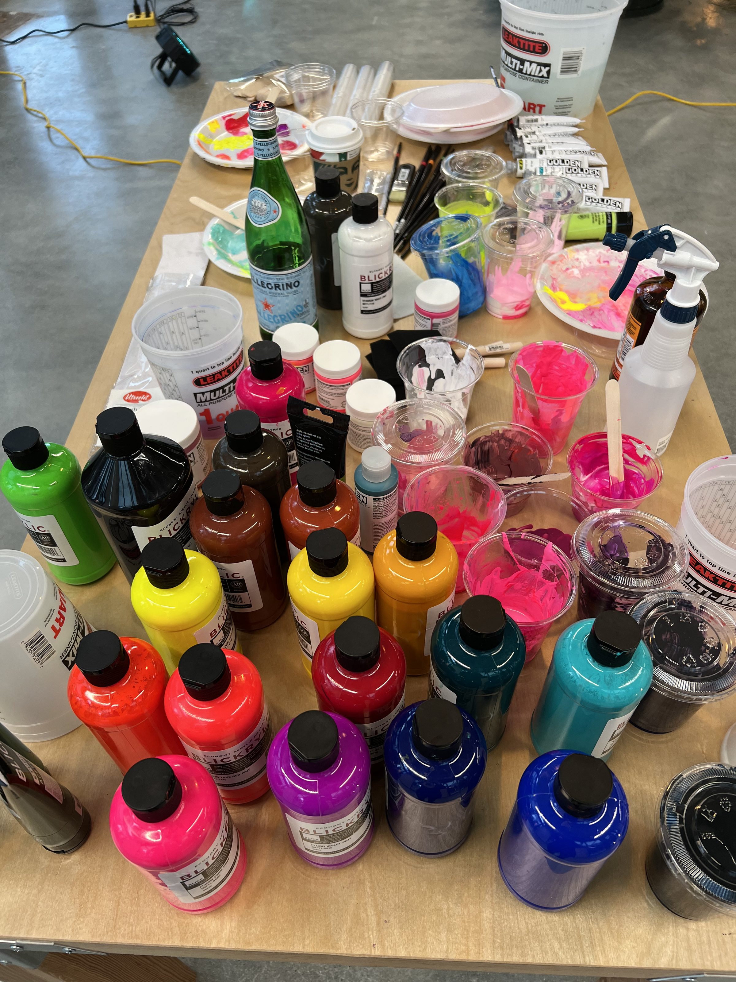 Overhead view of paint bottles and palette — the saturated colours of neon translated to acrylic.