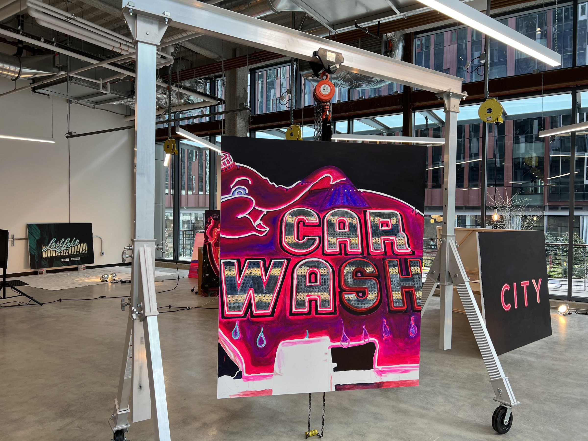 The CAR WASH panel hanging mid-air on the studio gantry hoist; Lost Lake behind on the floor, a CITY panel at right, South Lake Union outside the glass.
