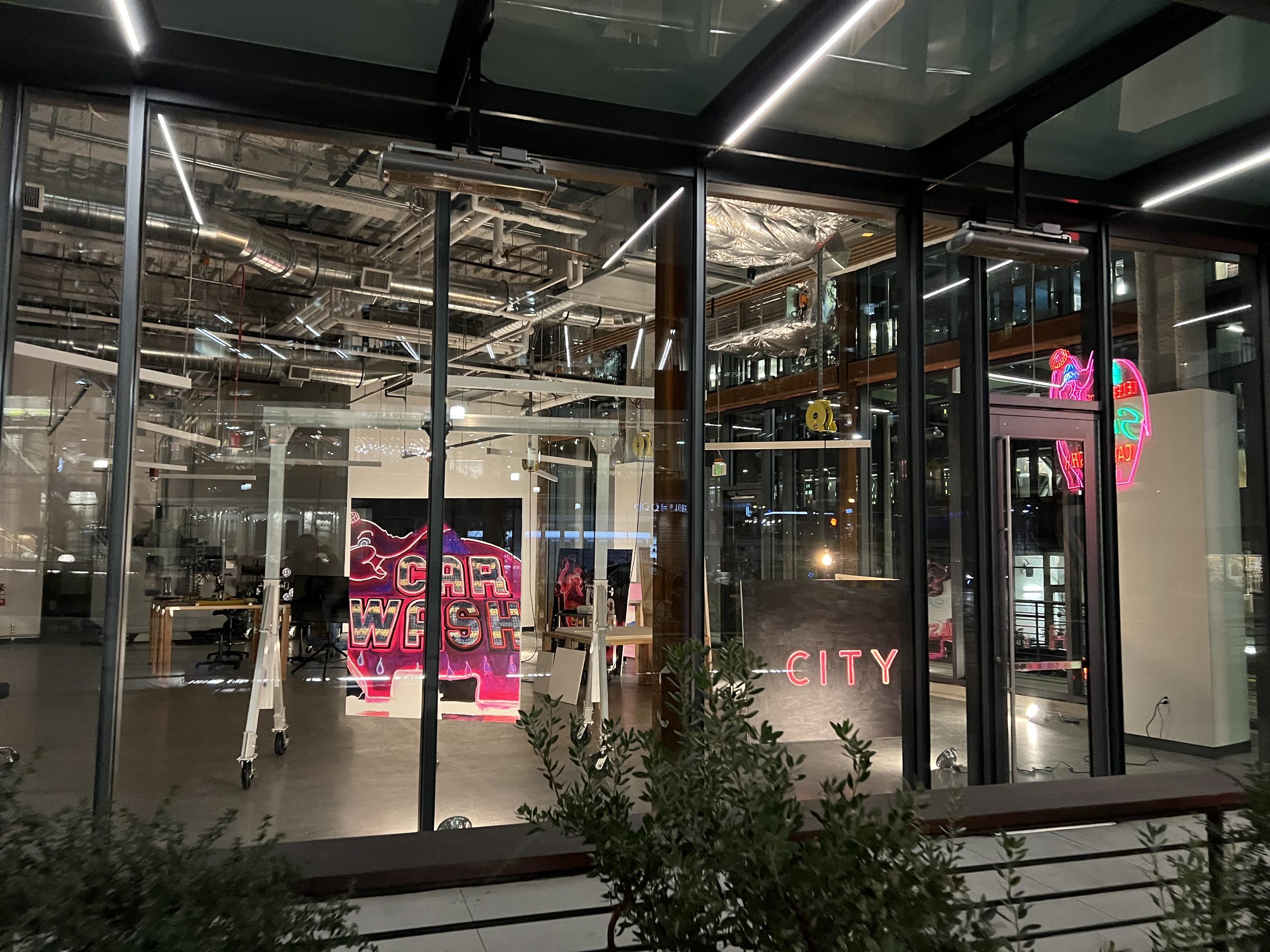The gallery viewed from the South Lake Union plaza at night — CAR WASH and CITY visible through the glass.