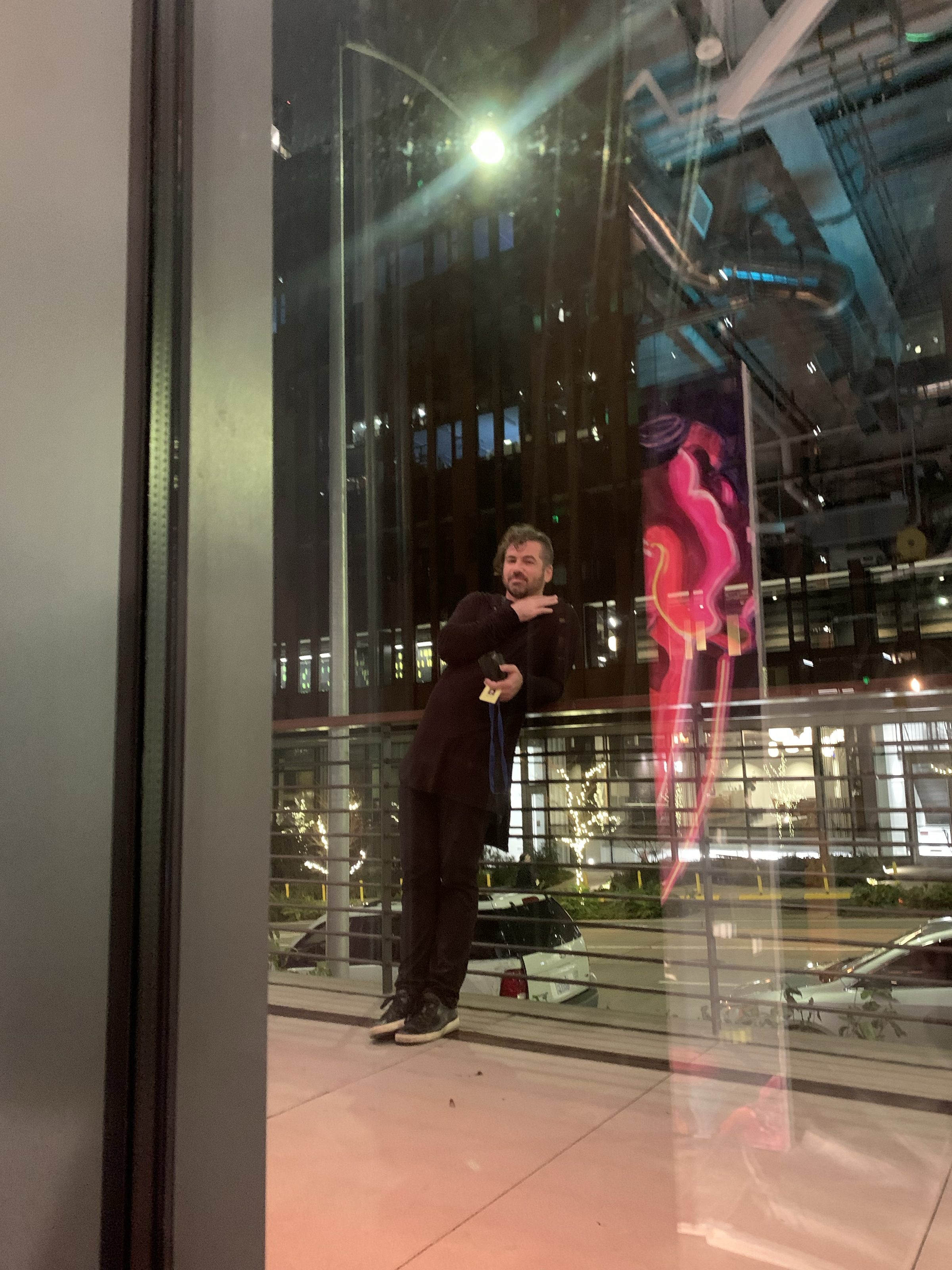Joshua Borsman at the City Light opening, the gallery glowing behind the glass.
